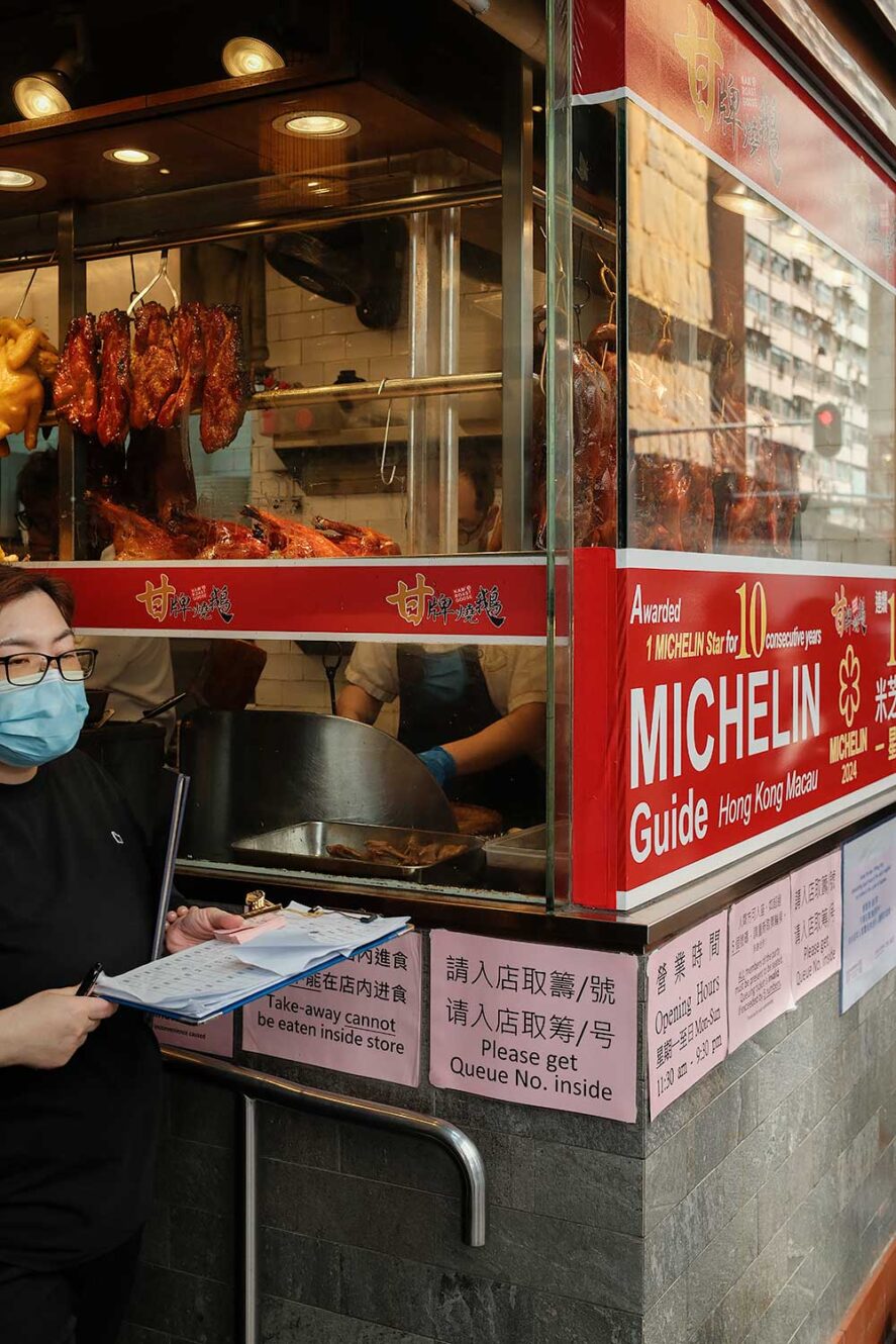 Vrouw regelt de rij met mensen die staan te wachten om te eten bij Michelin ster restaurant Kam's Roast Goose in Hong Kong, een van de beste restaurants